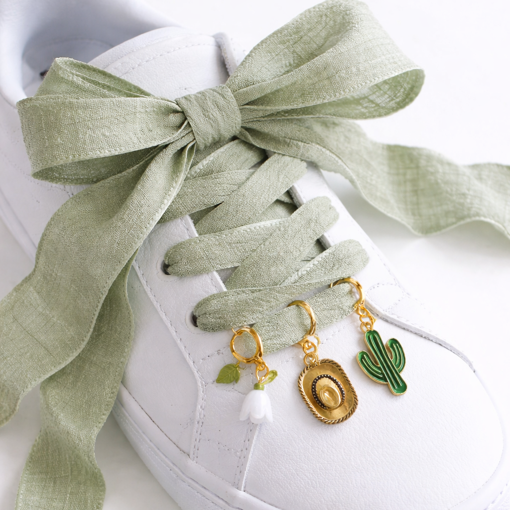 White sneaker with green ribbon and decorative charms on a white background