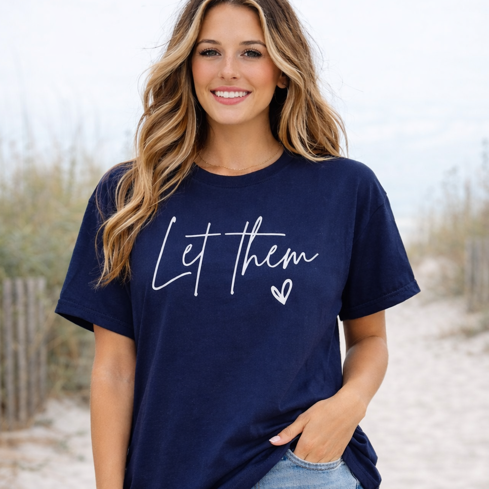 Woman wearing a navy blue t-shirt with 'Let them' text on a beach.