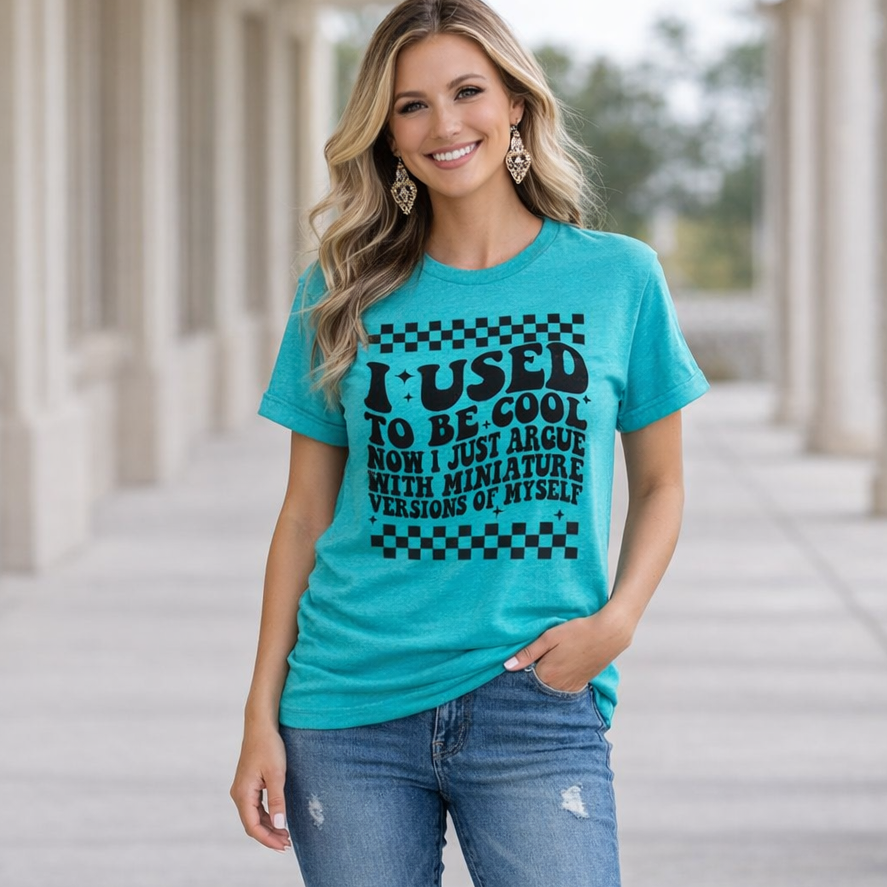 Woman wearing a turquoise t-shirt with text and ripped jeans on a stone pathway.