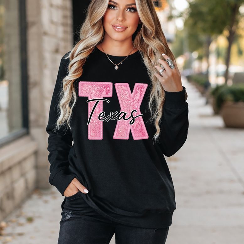 Woman wearing a black sweatshirt with 'TX Texas' in pink glitter on a sidewalk.