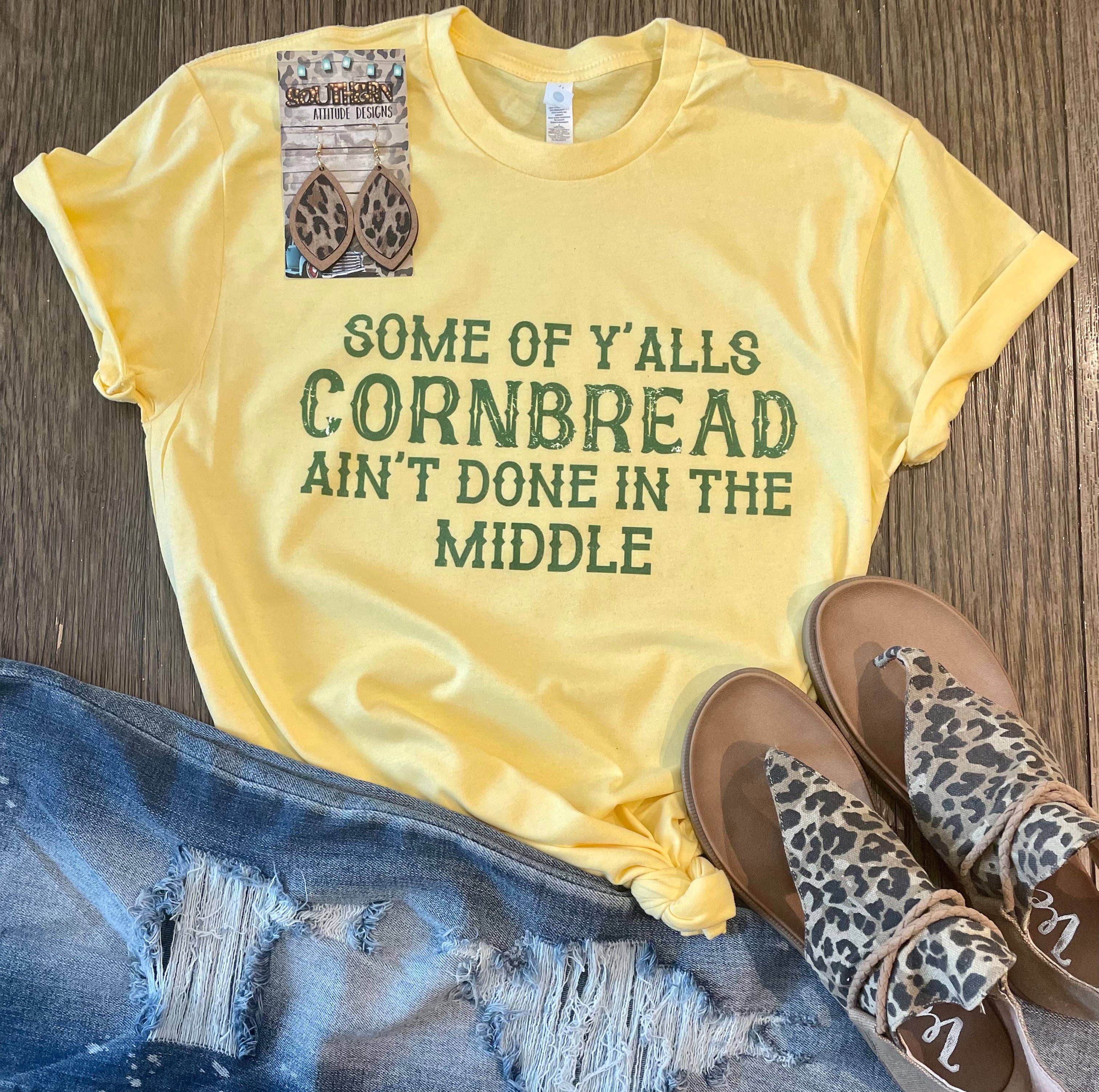 Yellow t-shirt with text, blue jeans, and leopard print sandals on a wooden surface