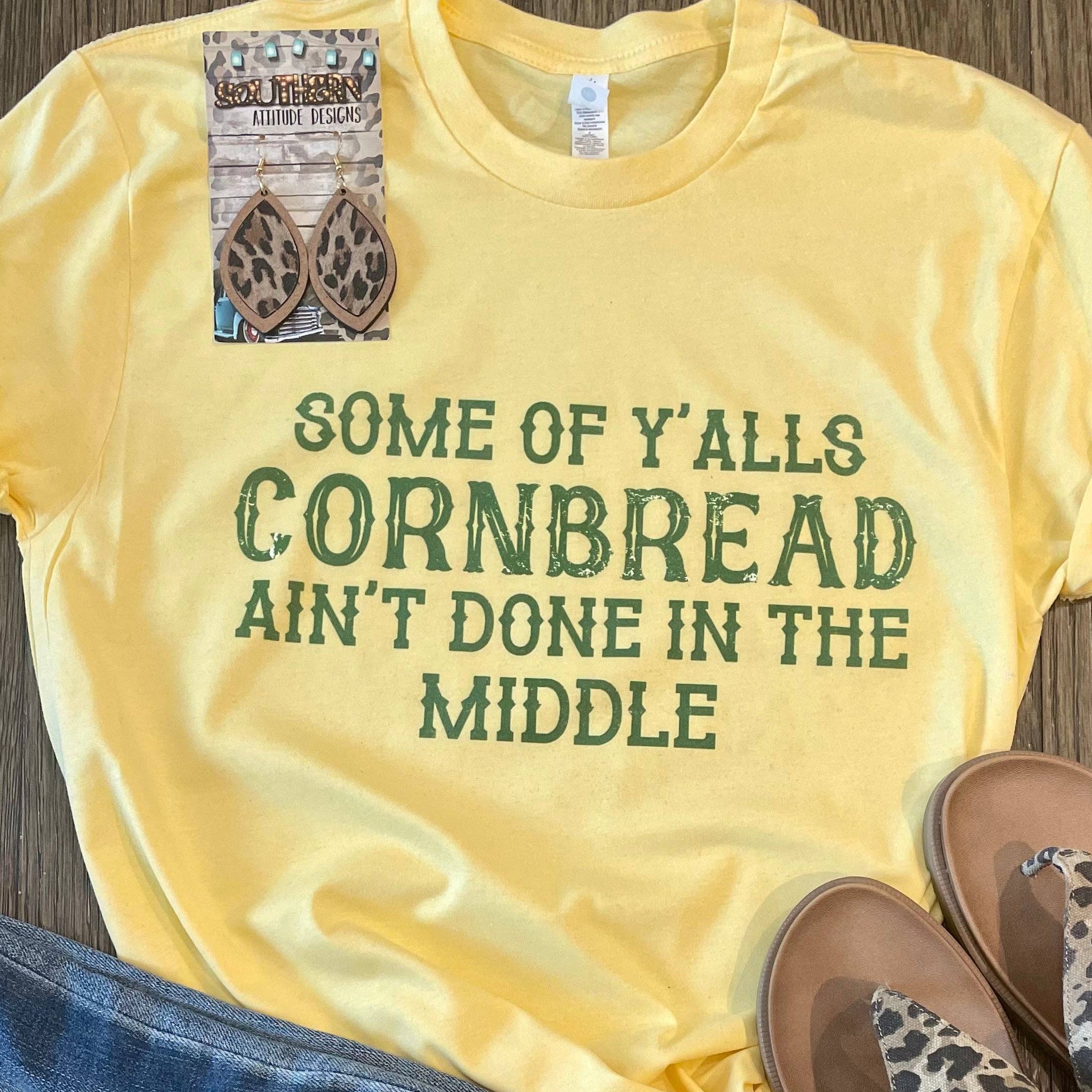 Yellow t-shirt with text, blue jeans, and leopard print sandals on a wooden surface