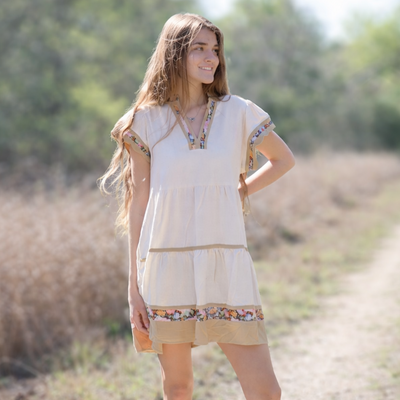 Woman in a light dress and cowboy boots standing on a dirt road with trees in the background