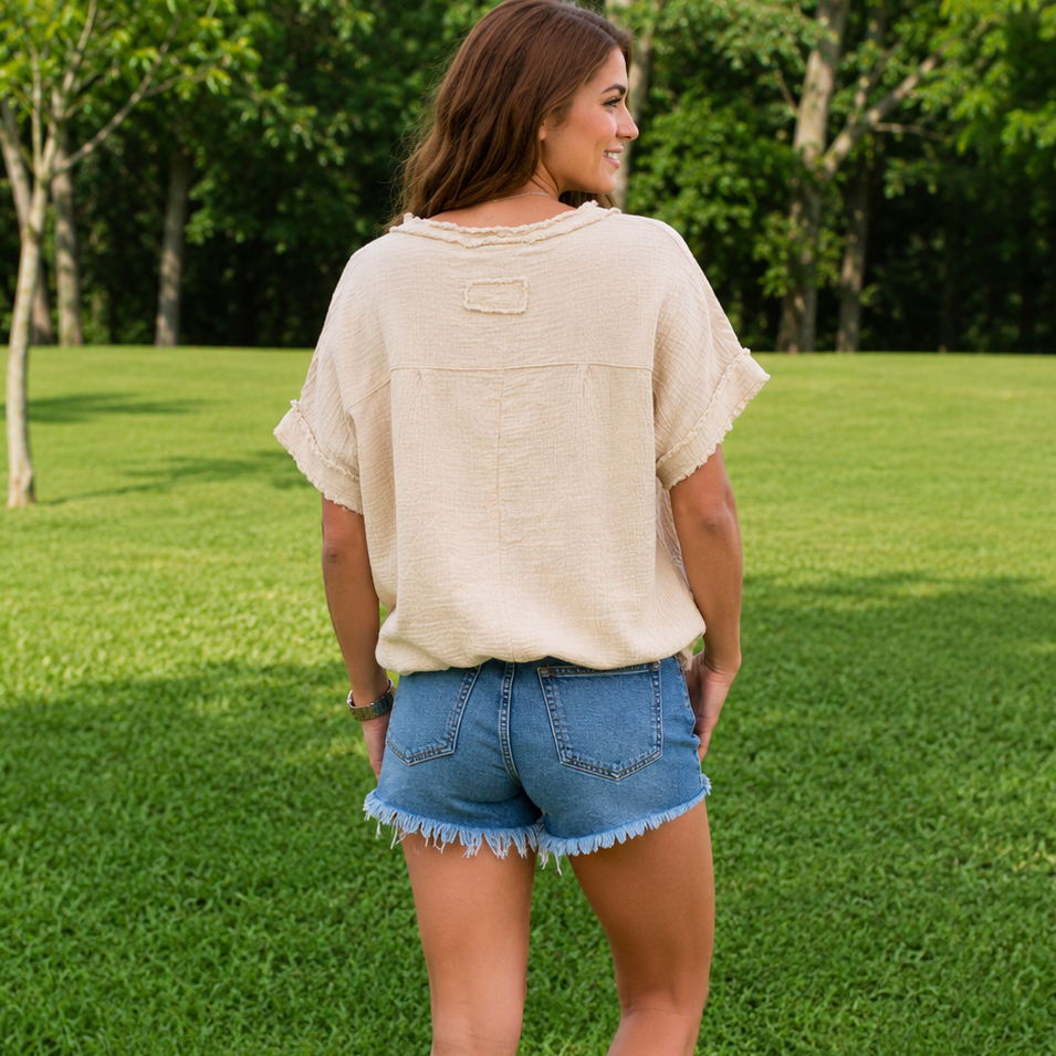 Woman standing on grass wearing a beige top and denim shorts