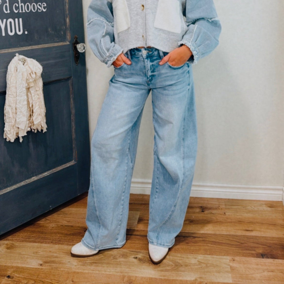 Woman wearing a light blue cardigan and jeans standing in front of a door with text.