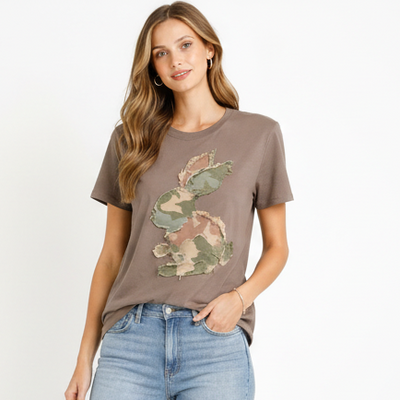 Woman wearing a brown t-shirt with a camouflage bunny design and blue jeans on a white background