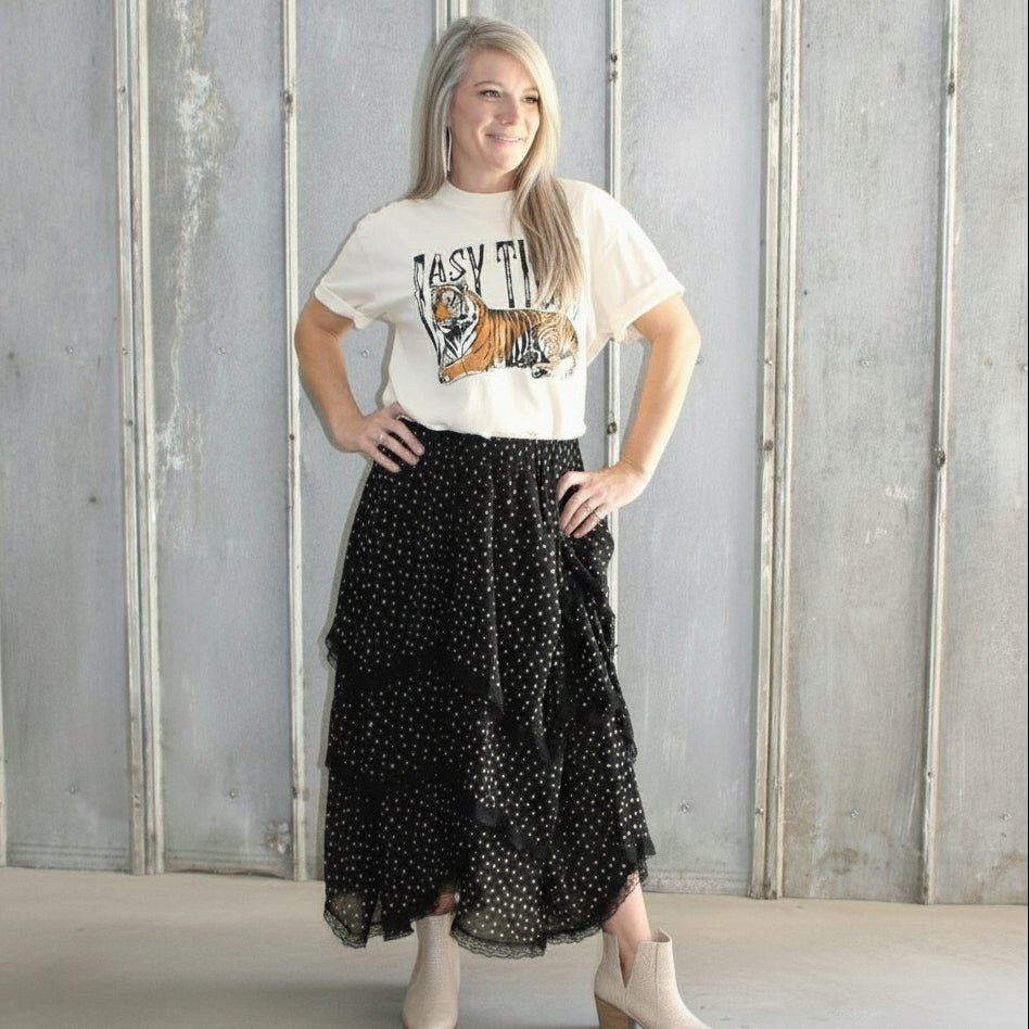 Person standing on a set of stairs wearing a white t-shirt and black patterned skirt.