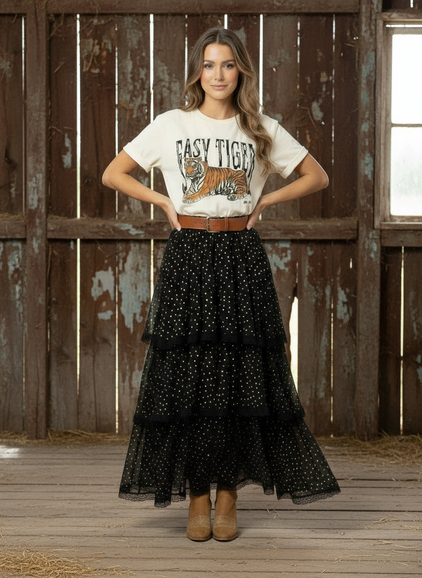Woman wearing a white t-shirt with a tiger graphic and a black tiered skirt in front of a rustic wooden wall.