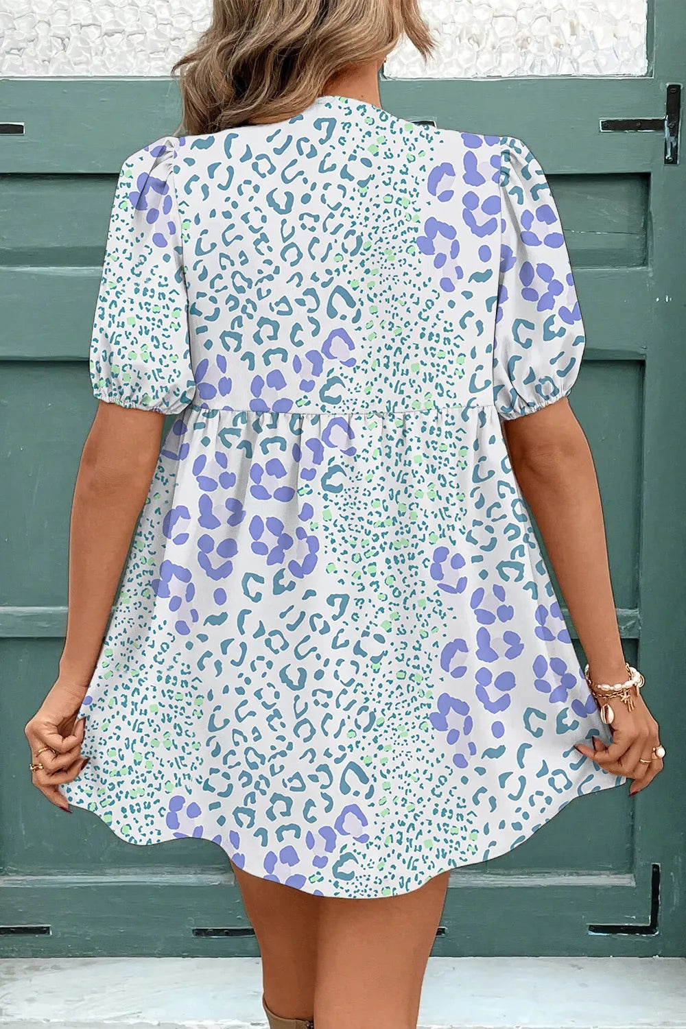 Woman wearing a patterned dress with a green and purple design against a green door.