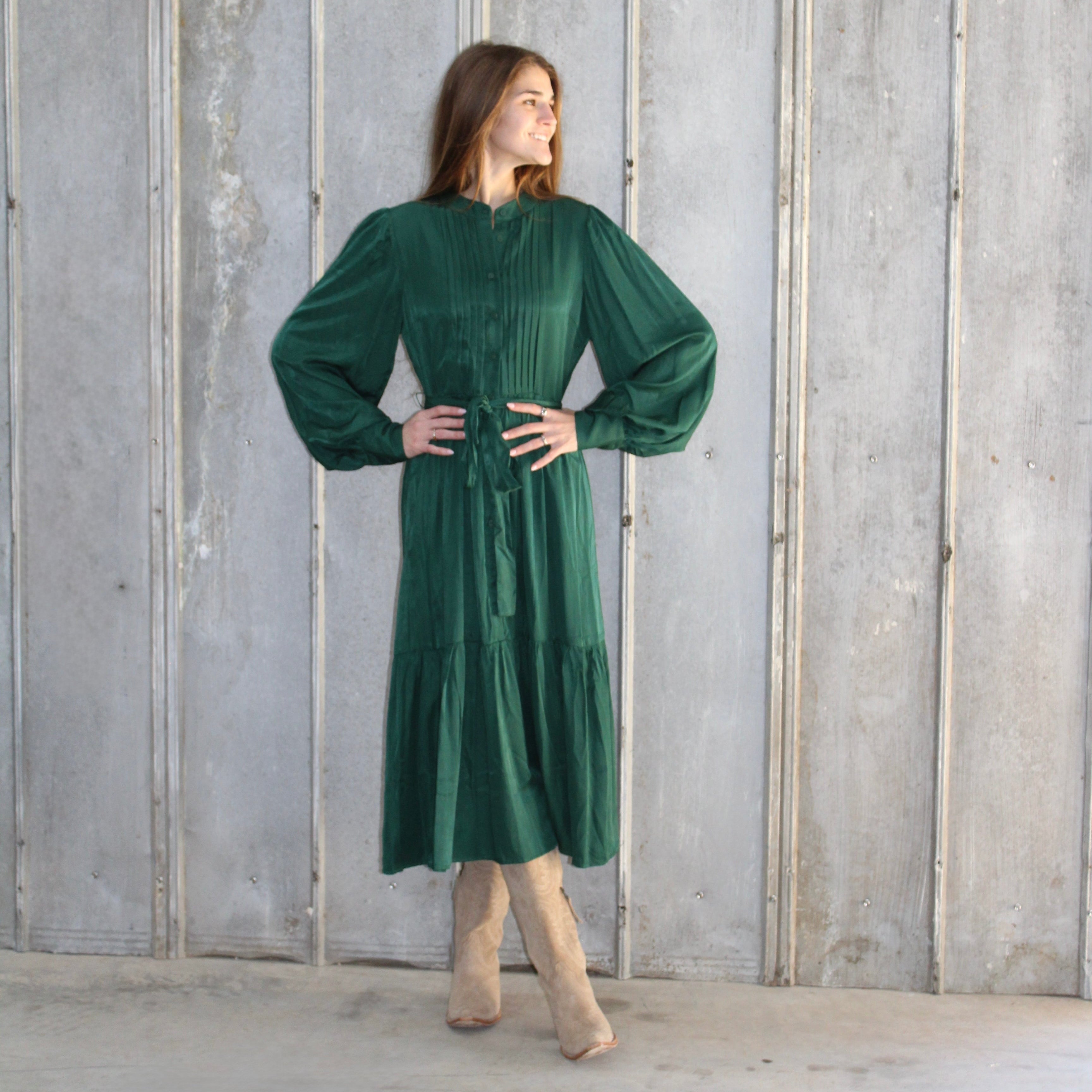 Woman wearing a green dress standing against a wooden paneled wall.