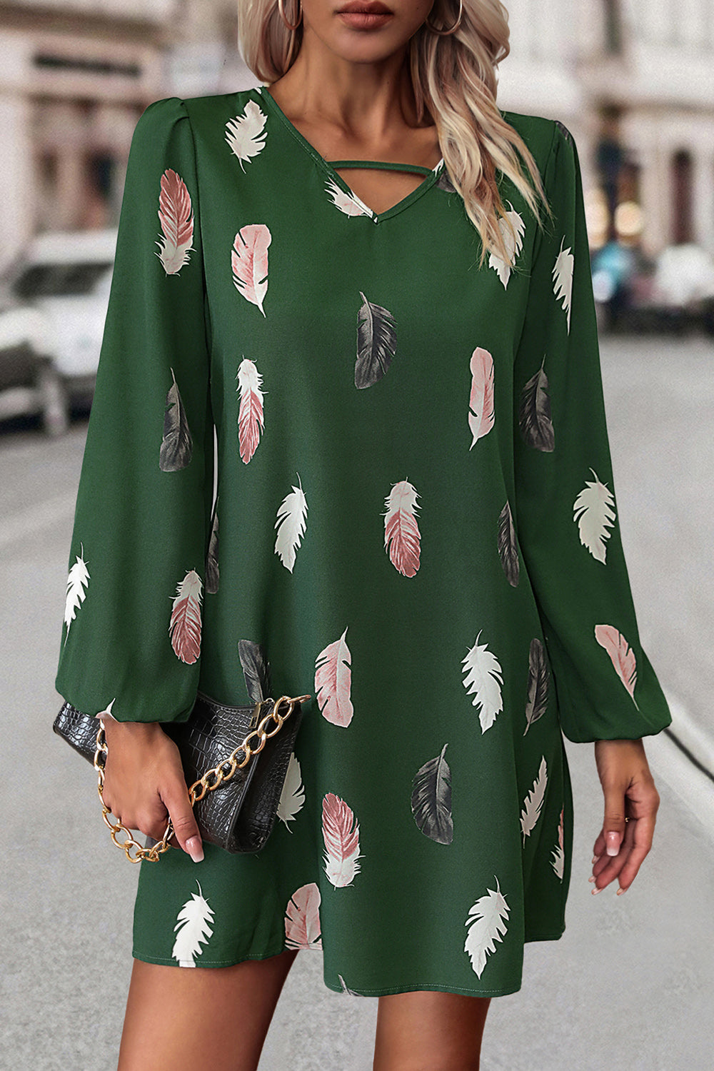 Woman wearing a green dress with feather pattern on a city street.