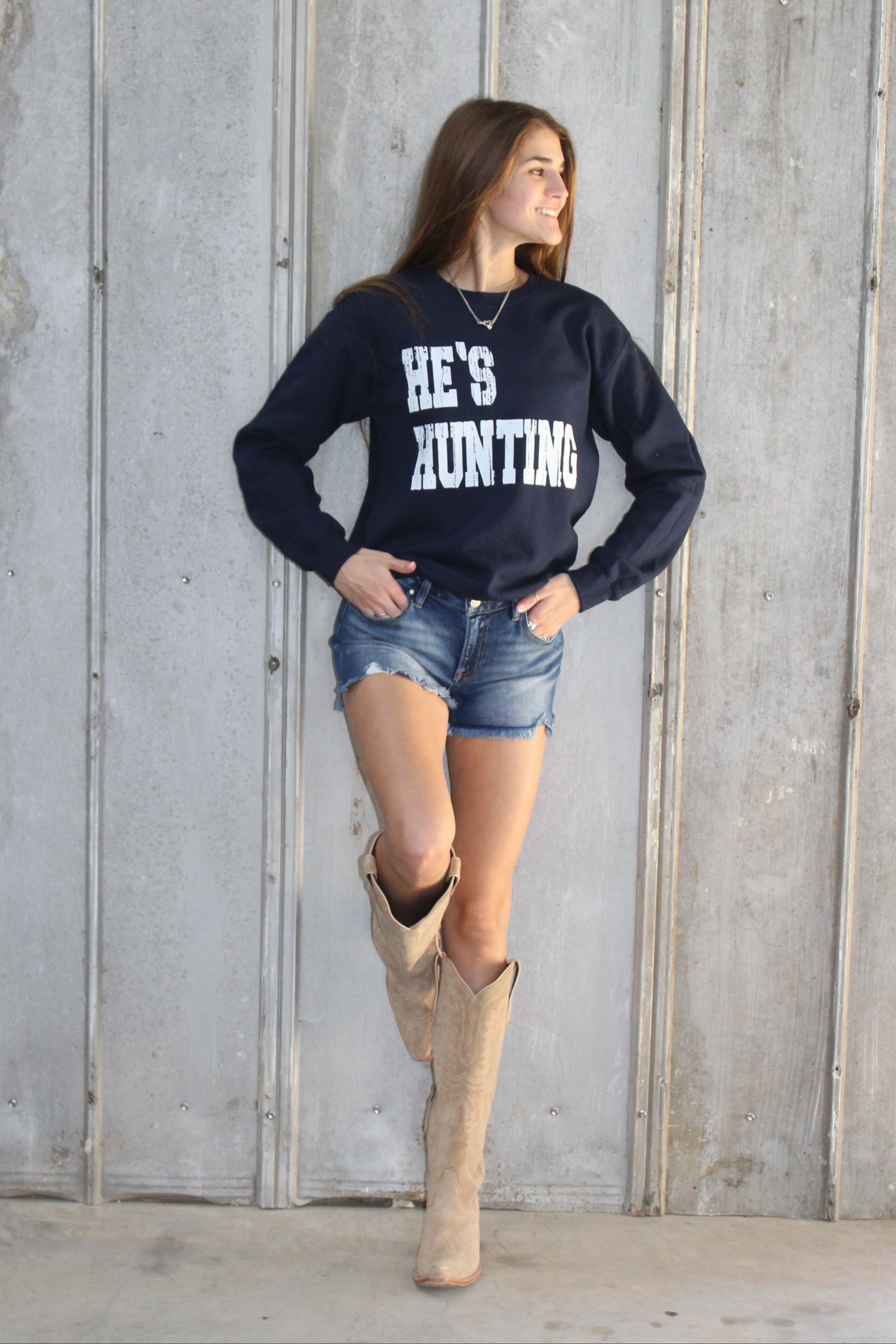 Person wearing a navy sweatshirt with text and denim shorts on a wooden floor.