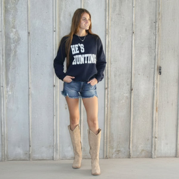 Person wearing a navy blue sweatshirt with text and denim shorts standing on a wooden floor.