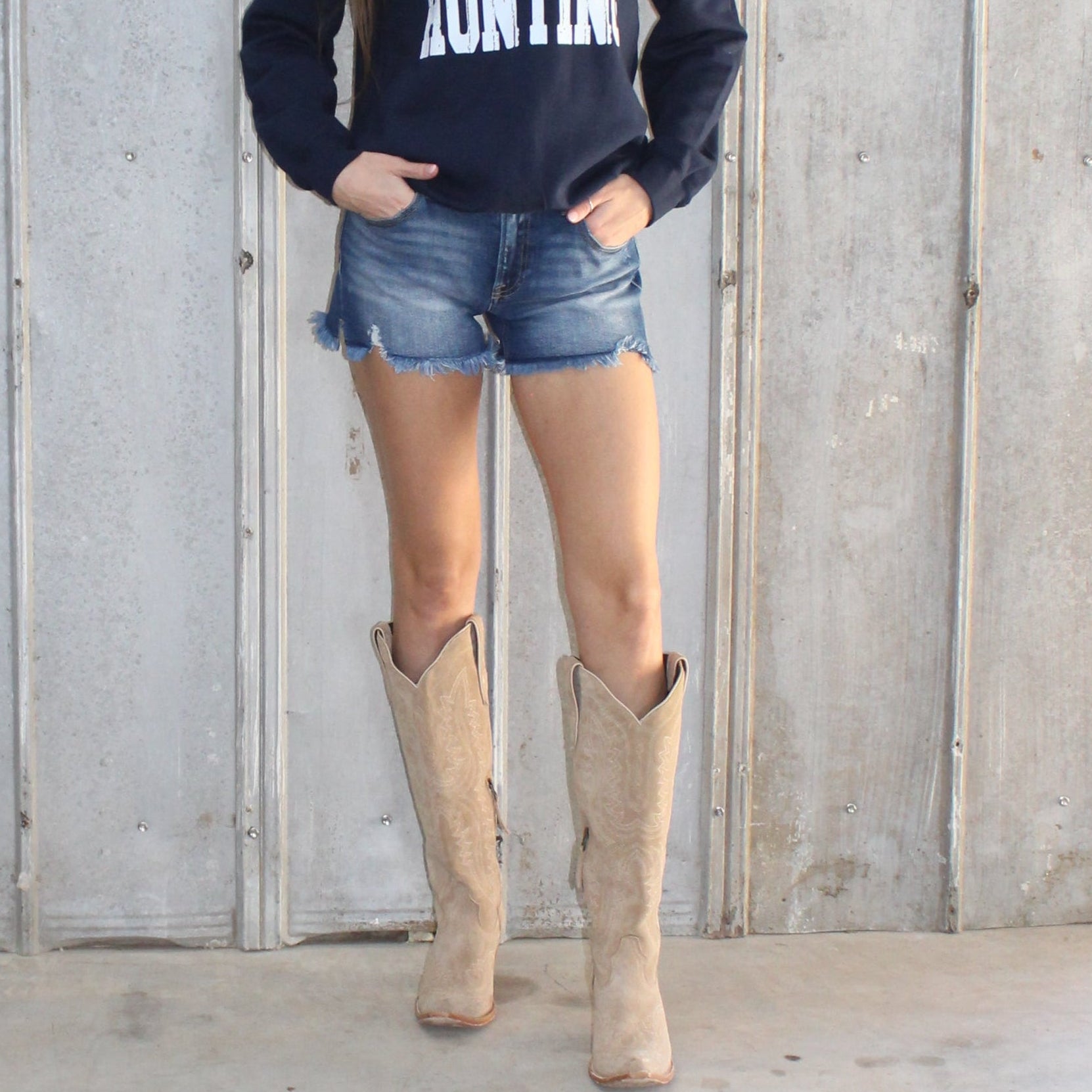 Person standing on a set of stairs wearing a dark hoodie and denim shorts.