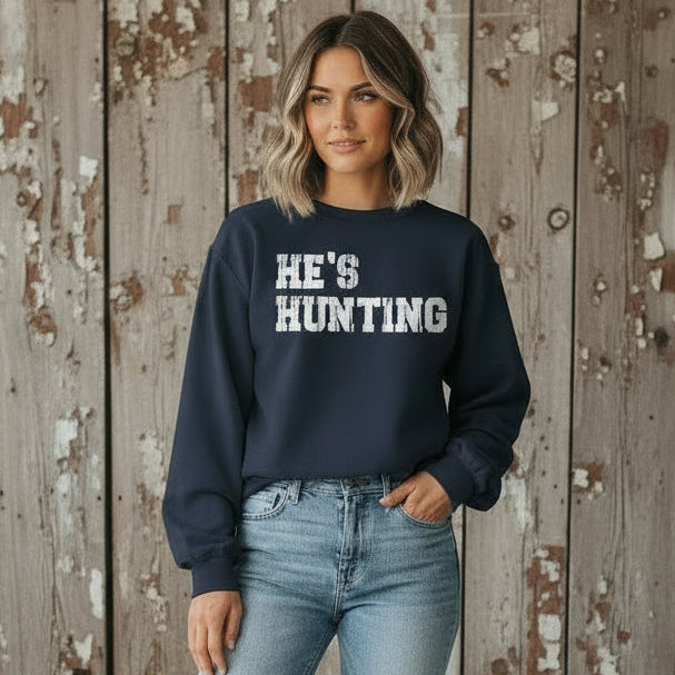 Person wearing a navy sweatshirt with 'HE'S HUNTING' text.