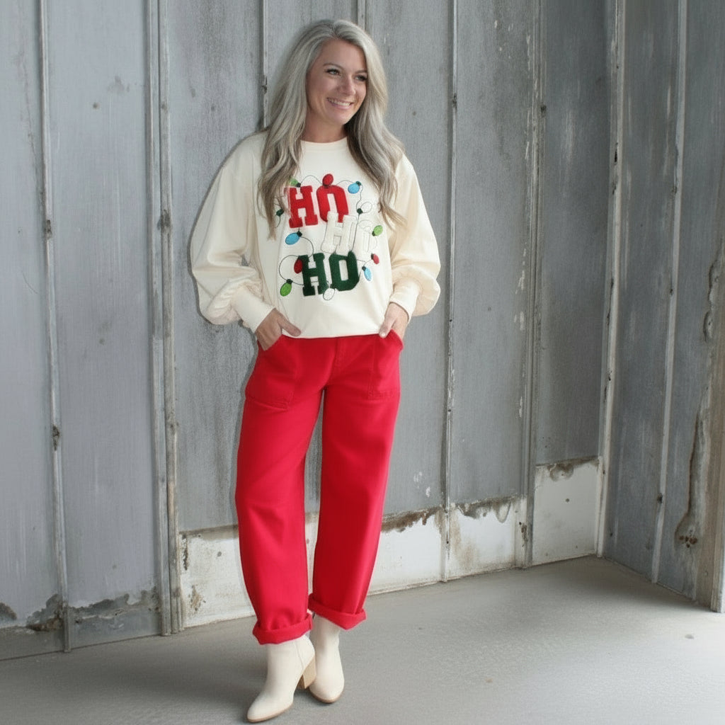 Person lying on a wooden deck wearing a white sweatshirt with text and red pants.