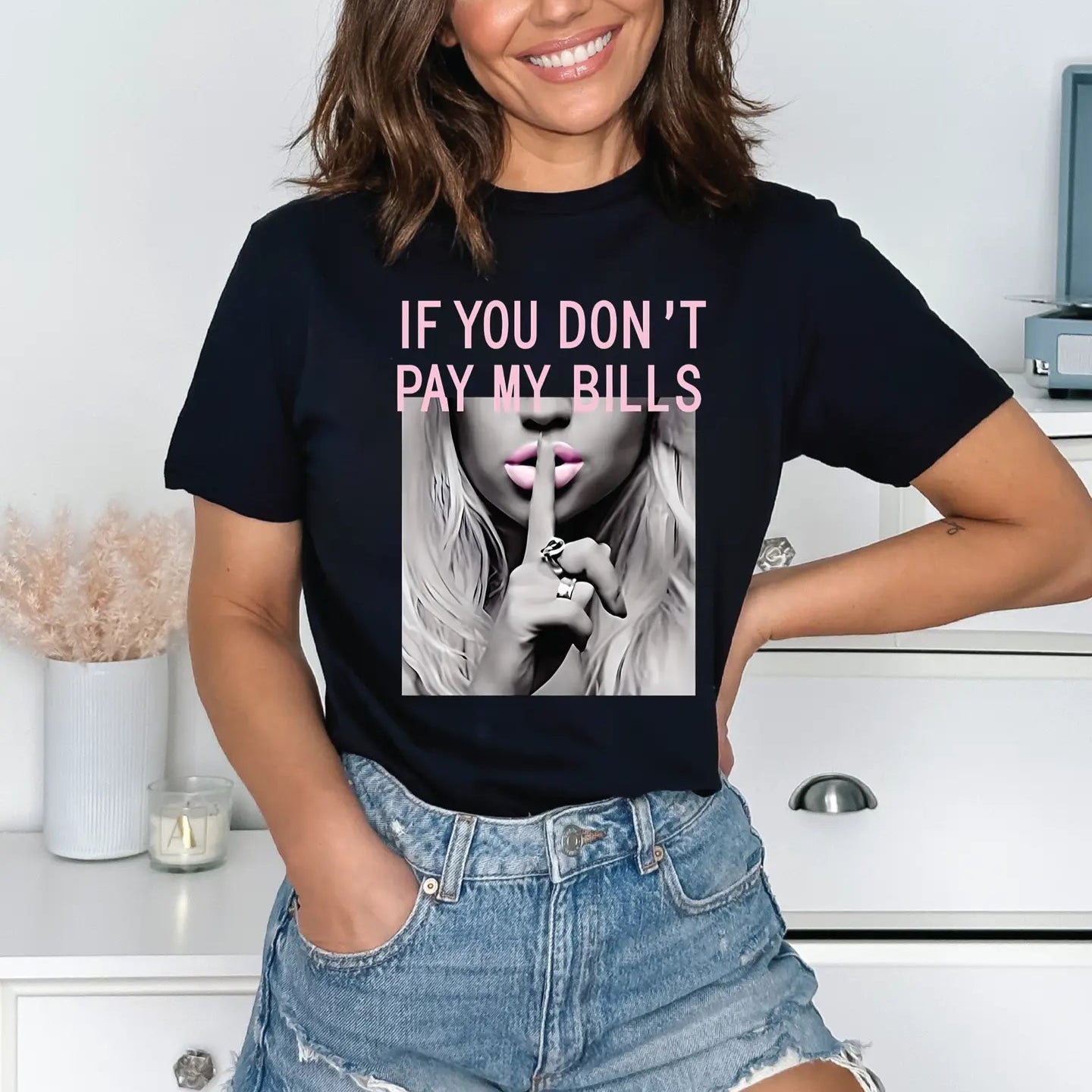 Woman wearing a black t-shirt with a graphic and text, standing in a room.
