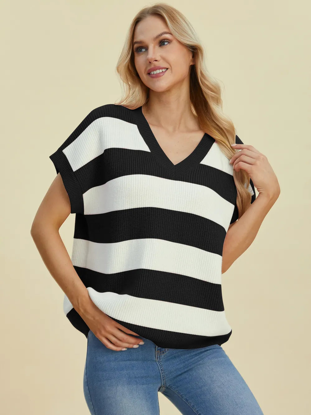 Woman wearing a black and white striped sleeveless top with blue jeans on a beige background