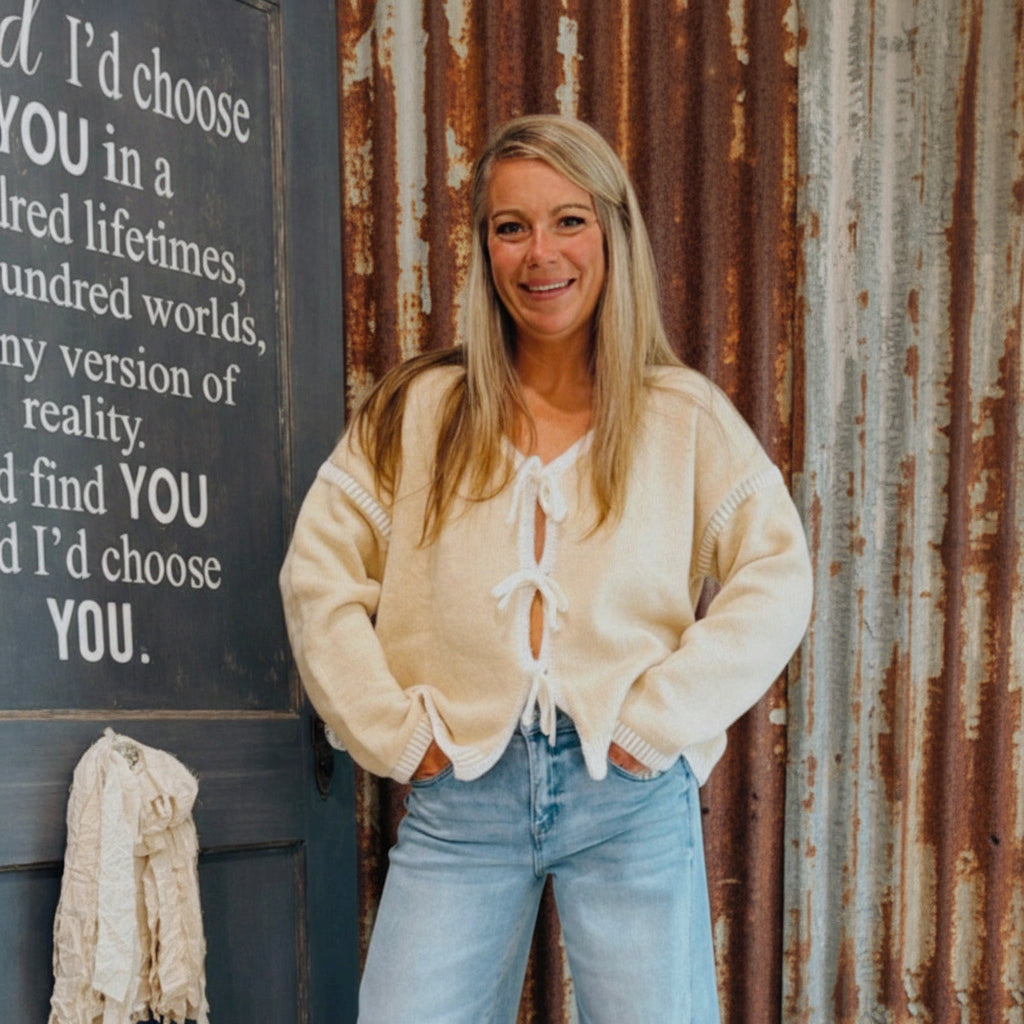 Woman wearing a beige cardigan and blue jeans standing in front of a chalkboard with text.