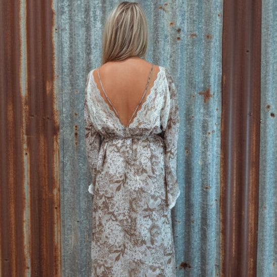 Woman wearing a lace dress with a backless design, standing in front of a wall with text and a coat rack.