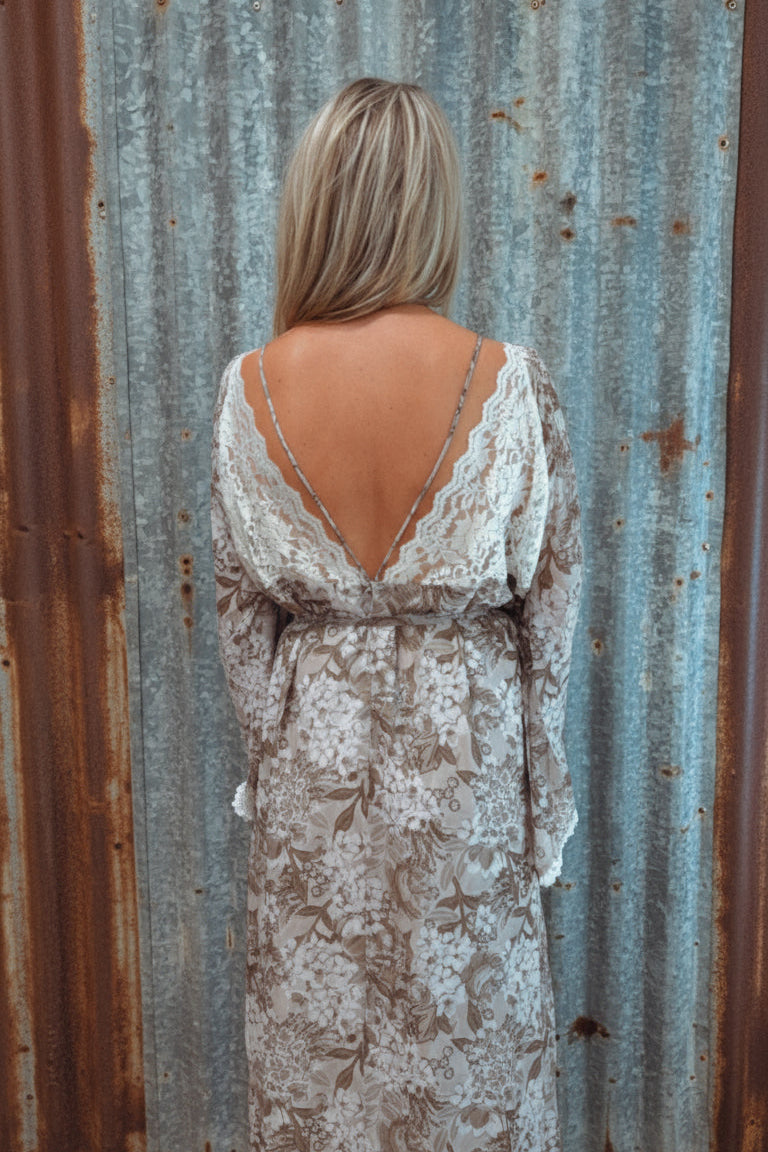 Woman wearing a lace dress with a backless design, standing in front of a wall with text and a coat rack.