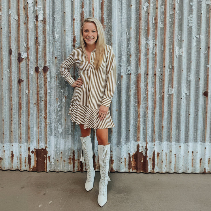 Woman in a striped dress and white lace boots standing in a room with wooden flooring.