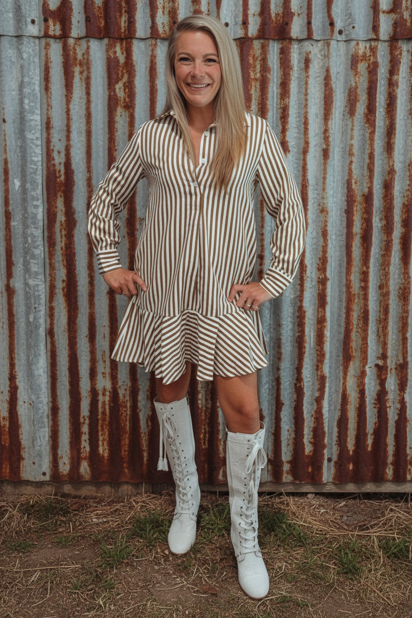 Woman in a striped dress and white boots standing in a room with a wooden floor and light blue wall.