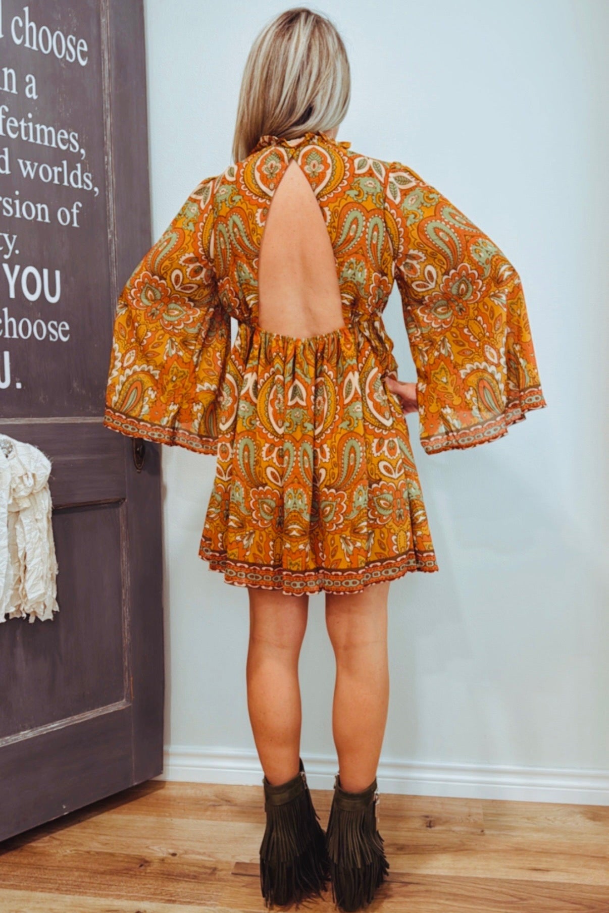 Woman wearing a patterned dress with open back in a room with a wooden floor and white wall.