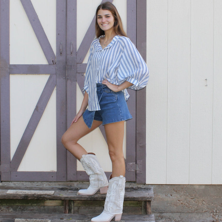 Woman standing on a wooden platform in front of a white building with a large wooden door.
