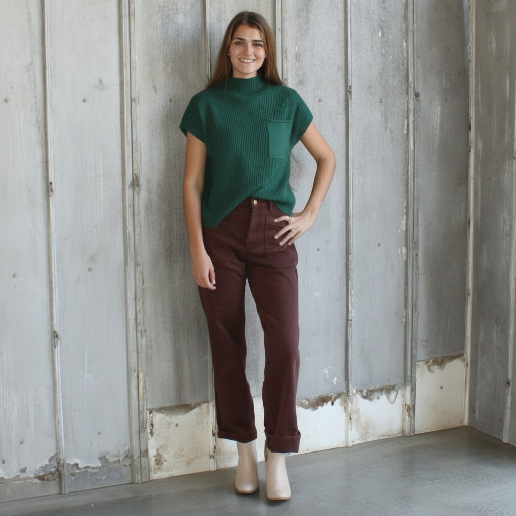 Woman in a green shirt and maroon pants standing in a rustic indoor setting with wooden walls.