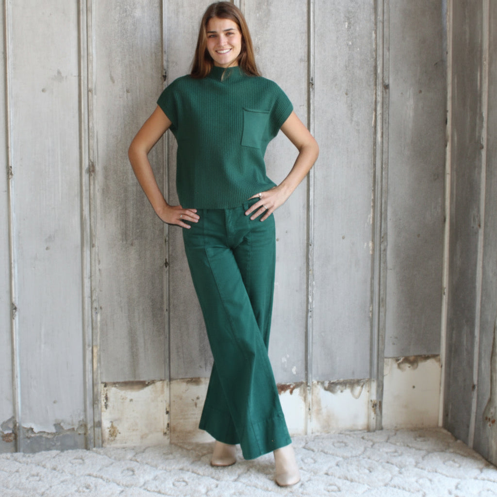 Woman wearing a green outfit standing against a wooden wall.