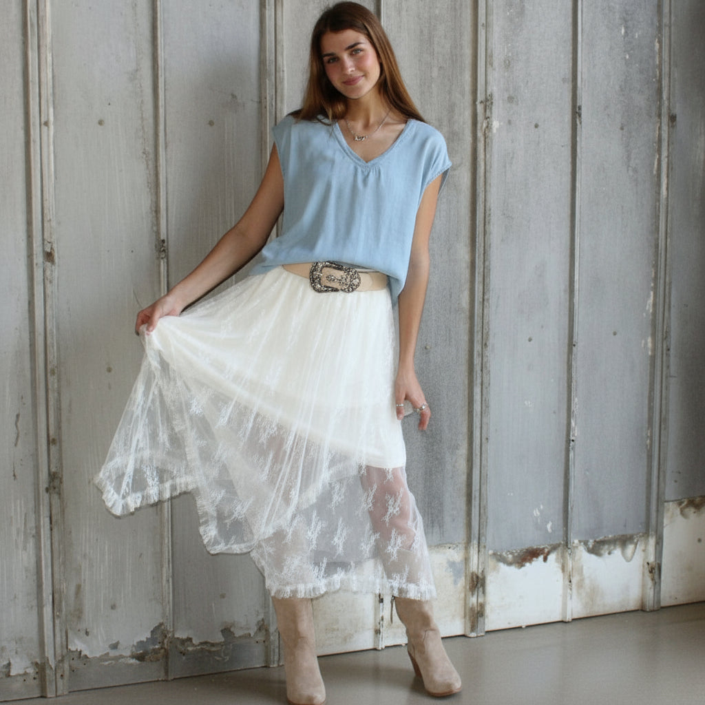 Woman wearing a light blue top and white lace skirt standing in a rustic wooden room.