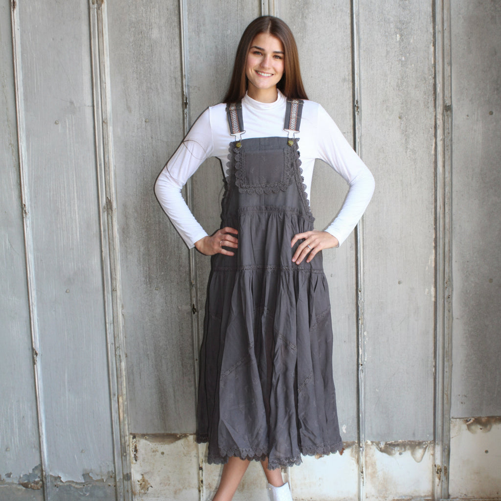 Woman wearing a gray overalls dress against a wooden wall.