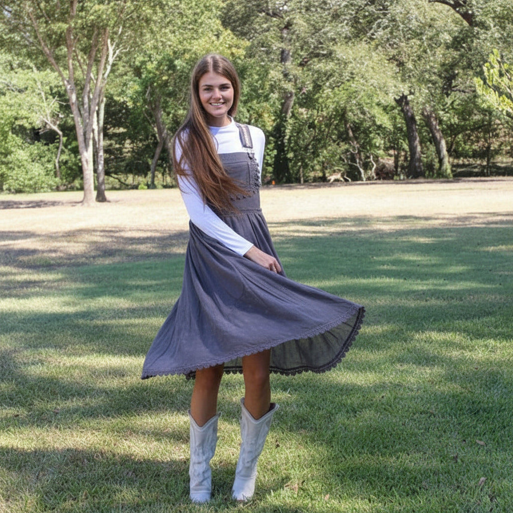 Woman in a dress and white boots standing in a park with trees and grass.