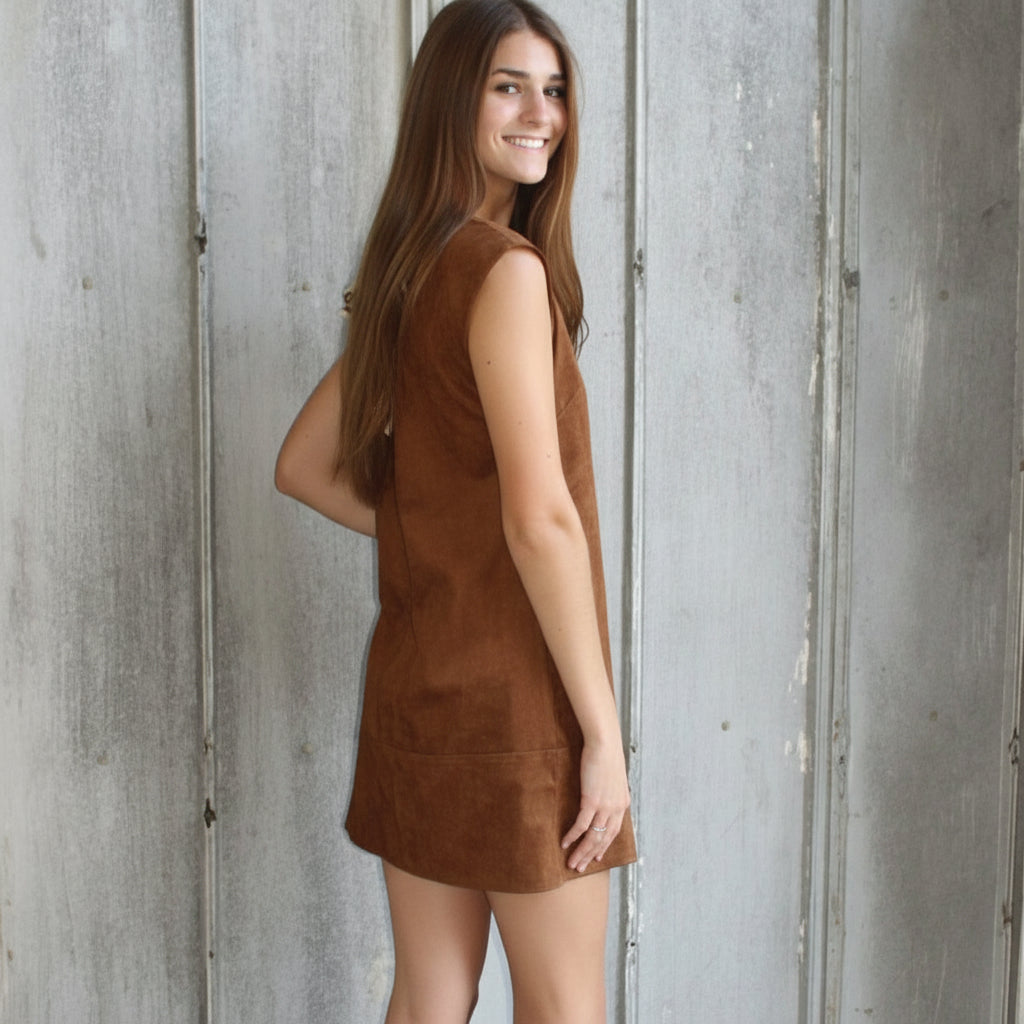 Woman in a brown dress standing against a textured wall.