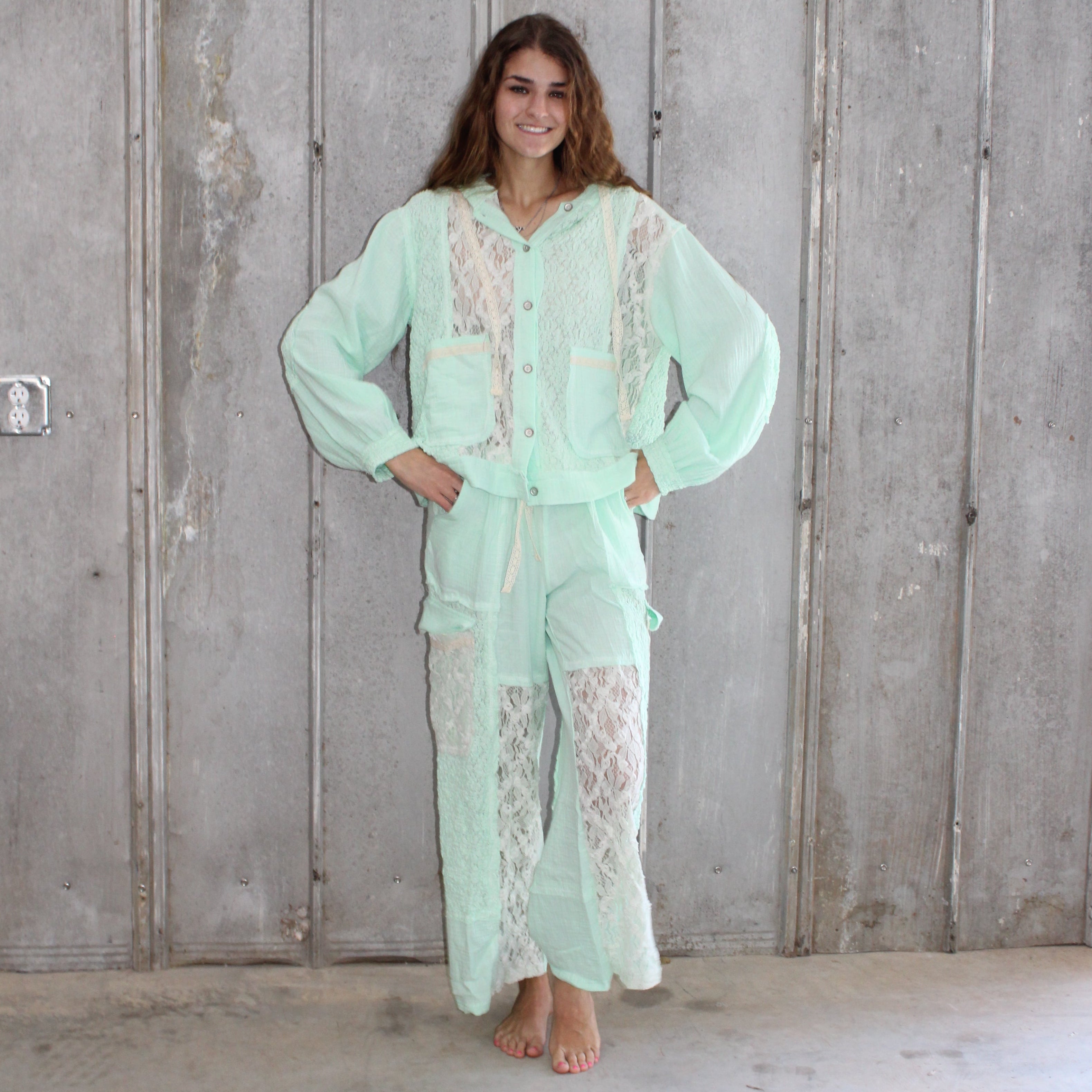 Person wearing a light green outfit standing against a wooden wall.