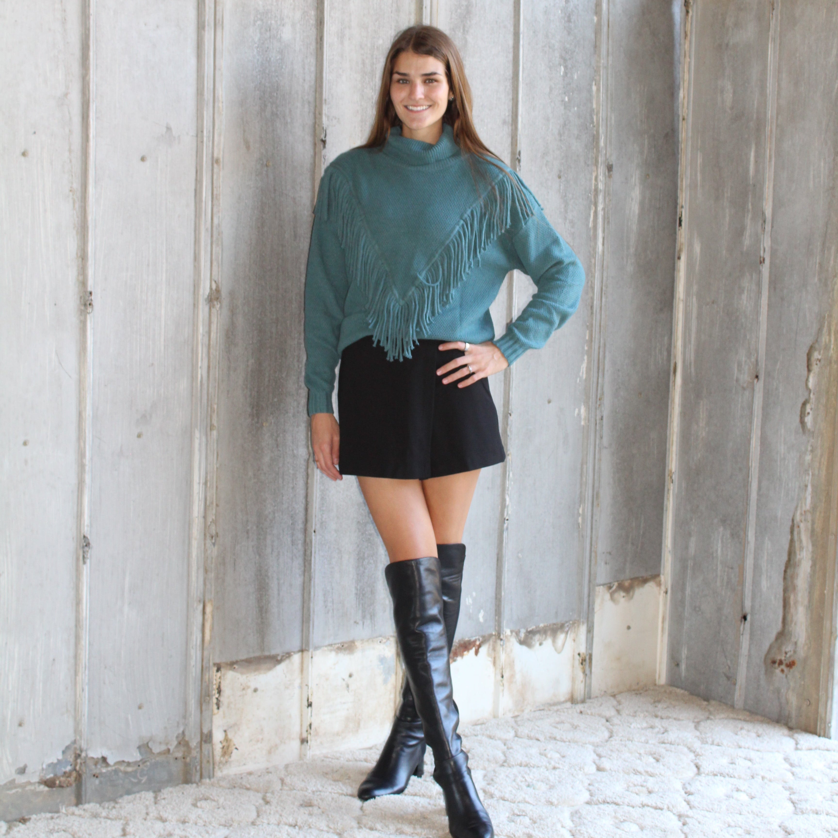 Woman in teal sweater and black skirt standing on a wooden staircase.