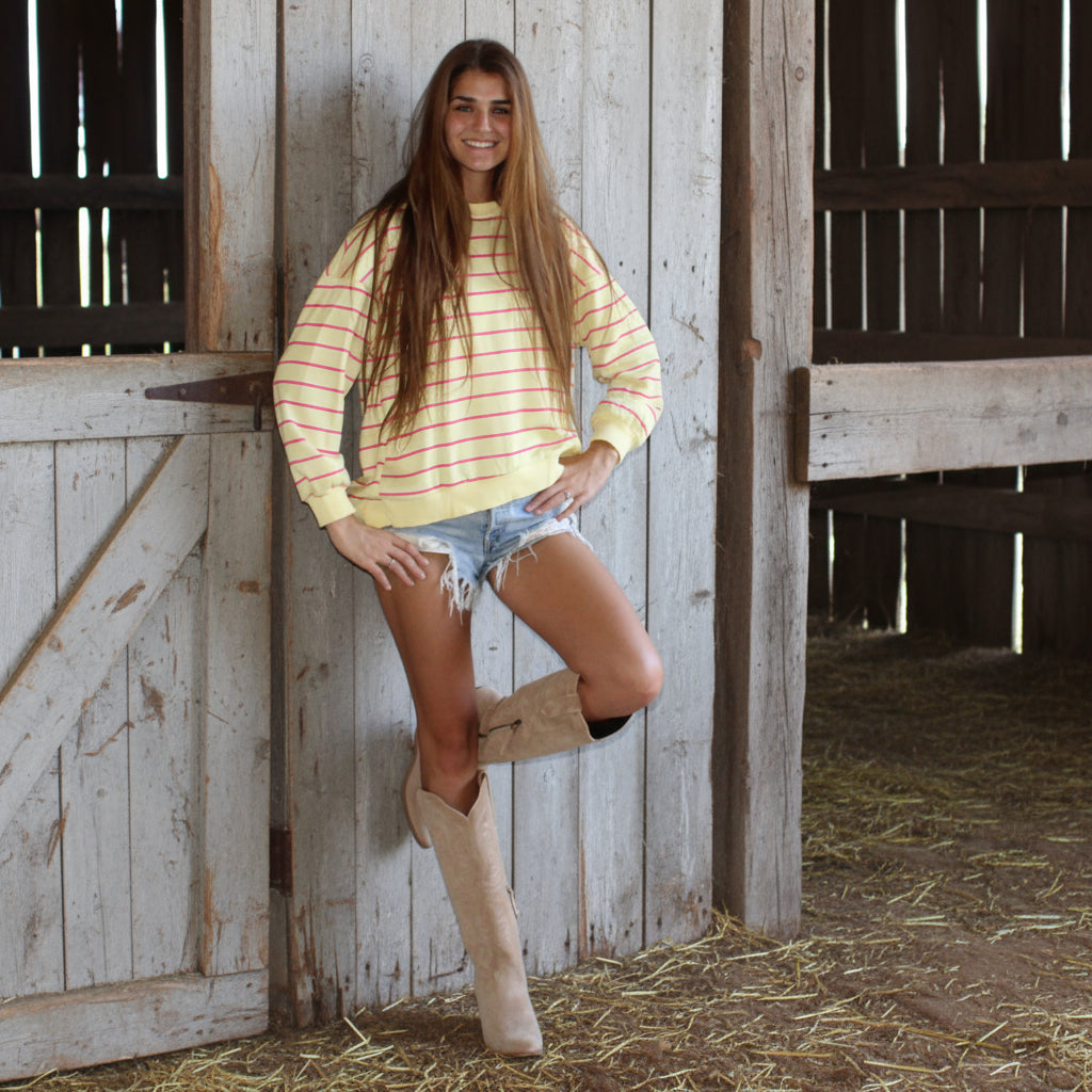 Woman in a striped shirt and shorts standing against a wooden wall.