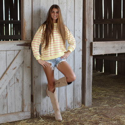 Woman in a striped shirt and shorts standing against a wooden wall.
