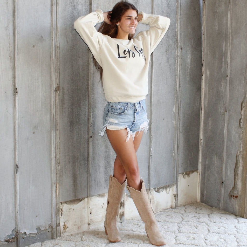 Woman in a white sweatshirt and denim shorts standing in a rustic wooden building.