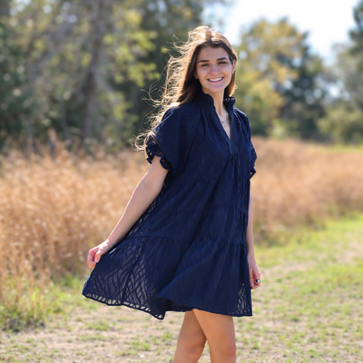 Woman in a navy dress standing in a field with trees in the background
