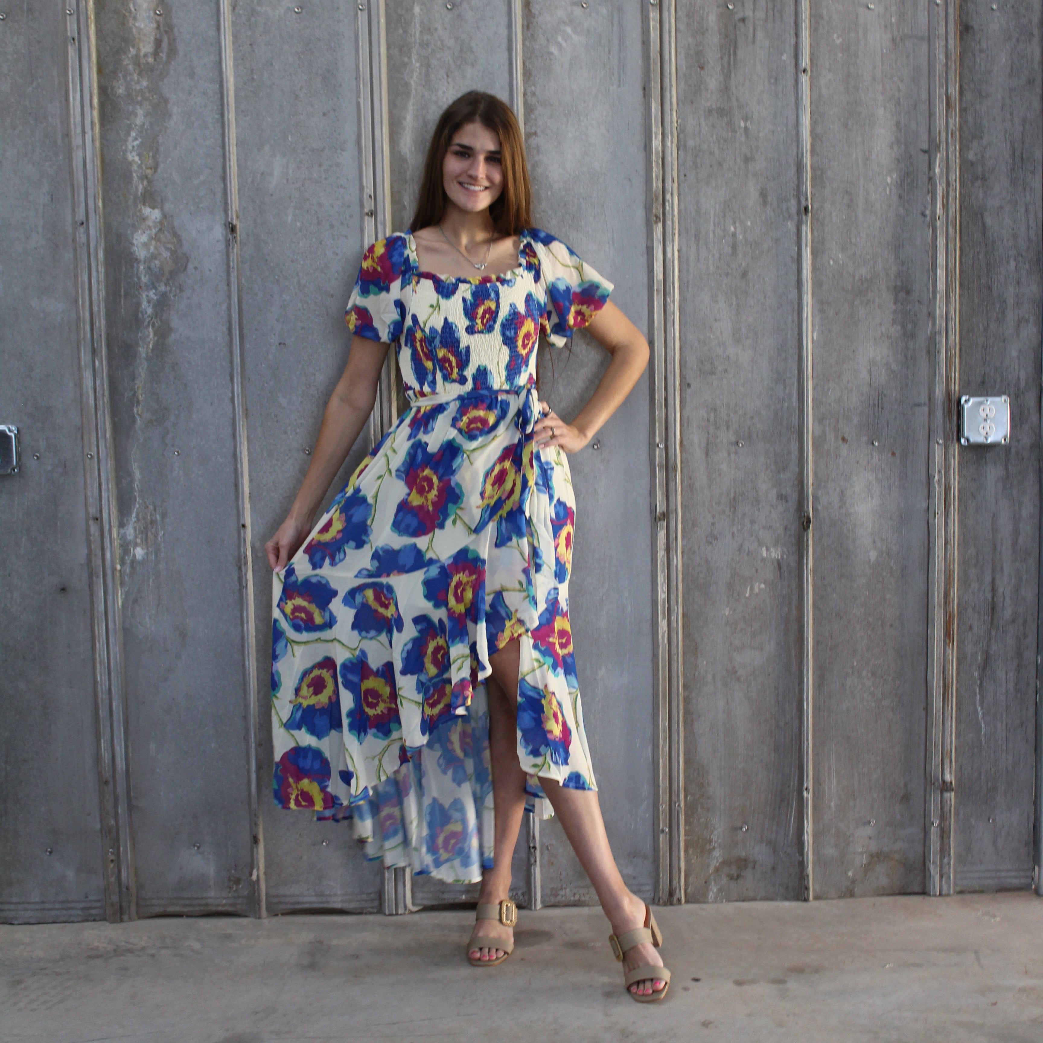 Woman in a colorful floral dress standing on a set of stairs.