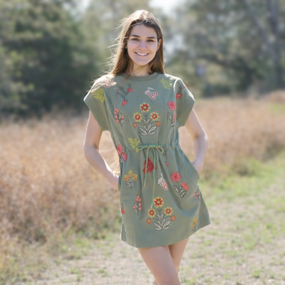 Woman wearing a green dress with floral embroidery standing in a natural setting.