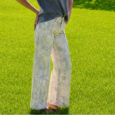 A woman stands on a bright green lawn in a park, wearing a dark gray short-sleeve t-shirt and light beige wide-leg pants.