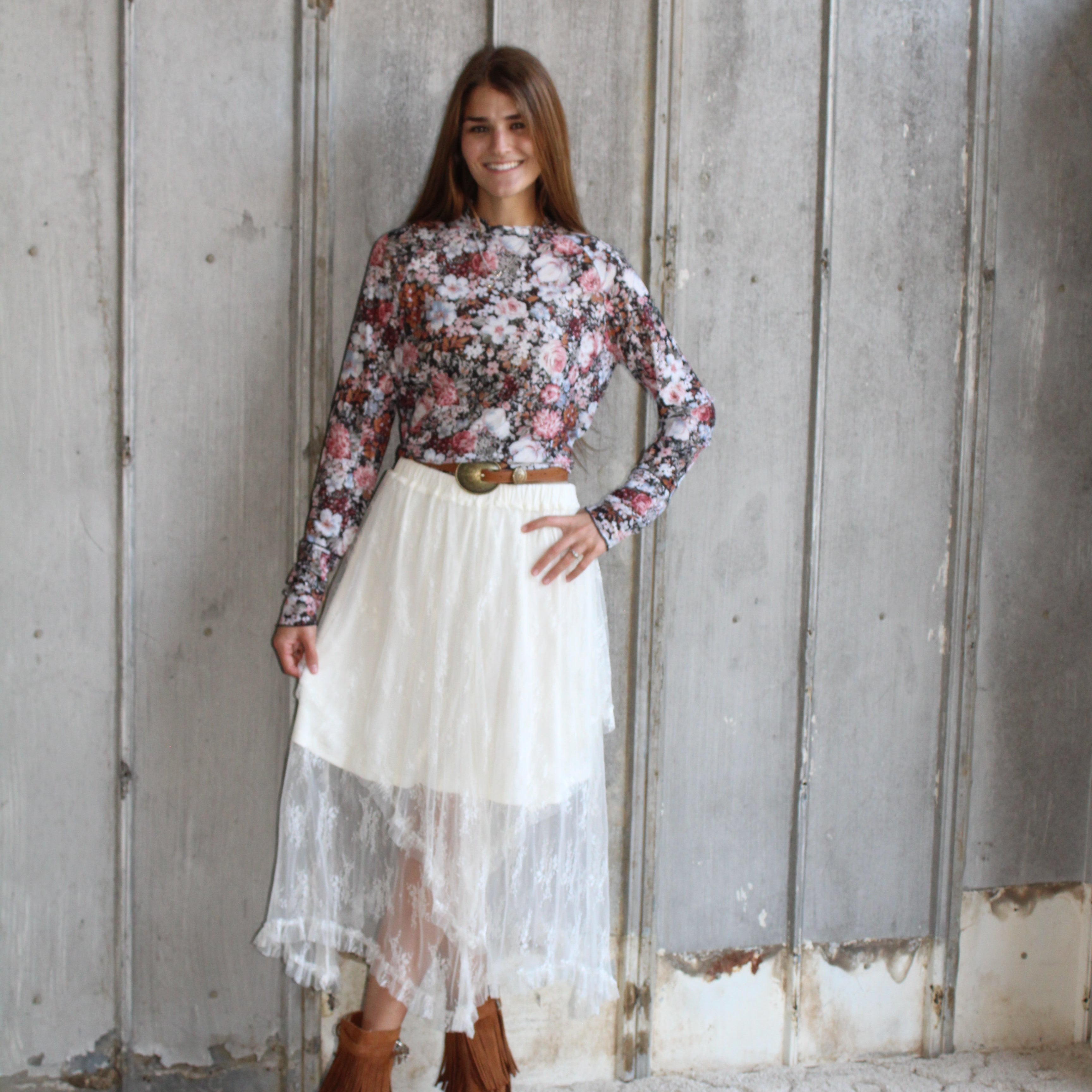 Woman in a floral top and white skirt standing on a wooden floor.