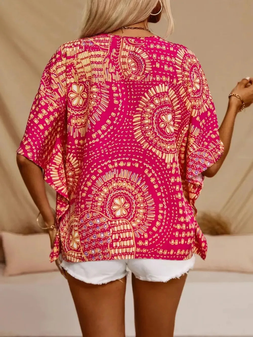 Person wearing a bright pink and yellow patterned top with white shorts on a beige background