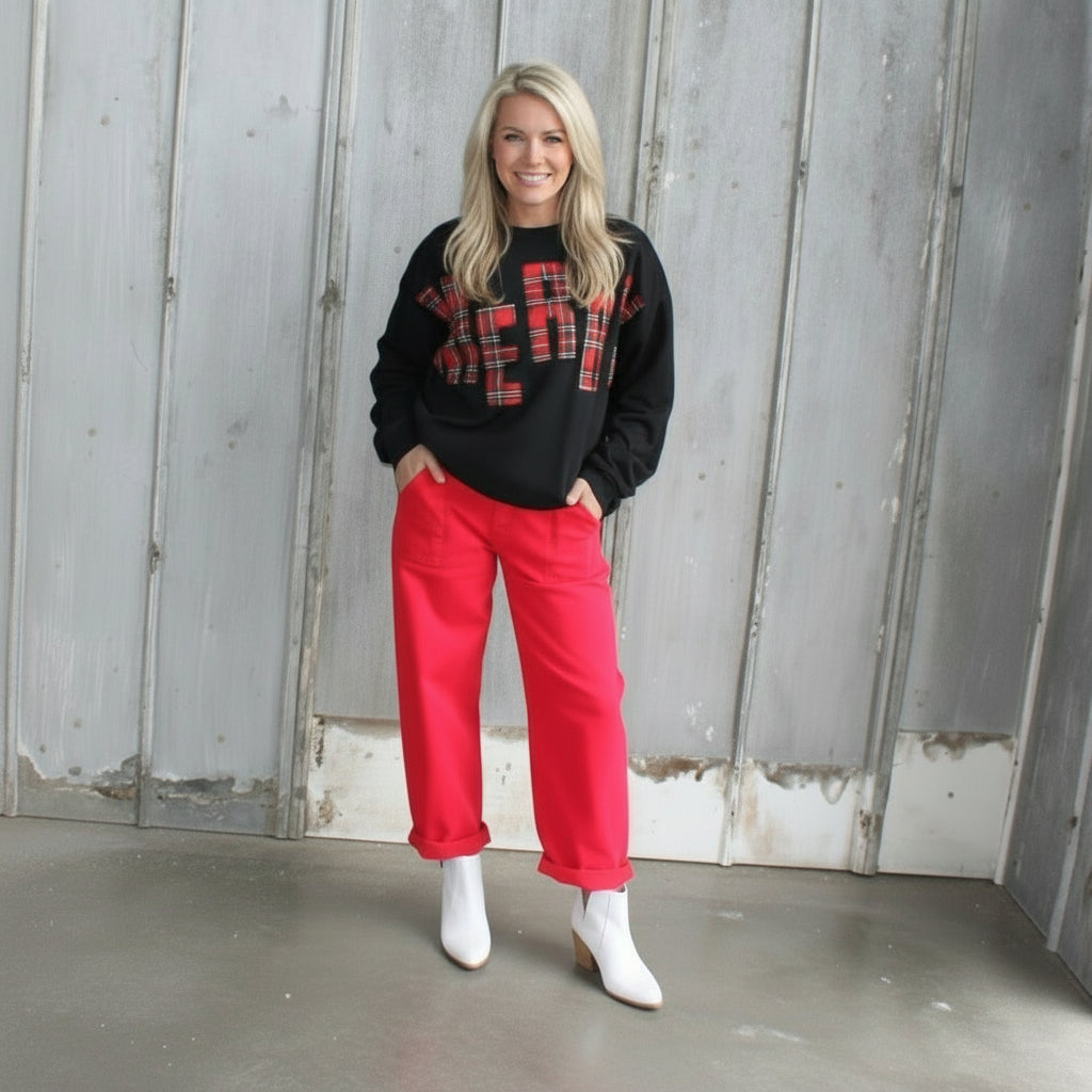 Person wearing a black sweatshirt with red text and red pants standing in front of a rustic wooden wall.