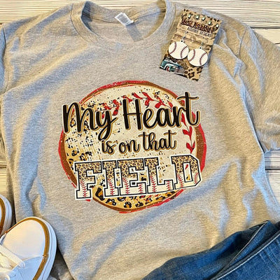 T-shirt with 'My Heart is on that Field' design, paired with jeans and sneakers on a wooden surface.
