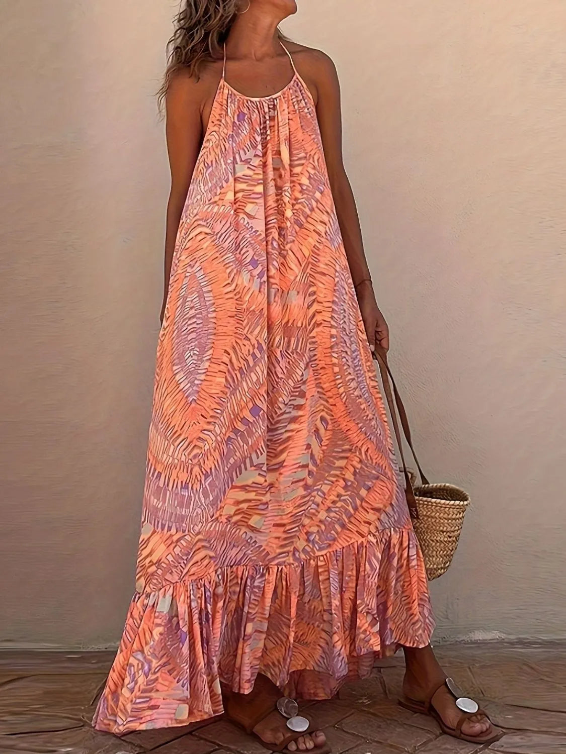 Woman wearing a long, patterned orange dress against a beige wall.