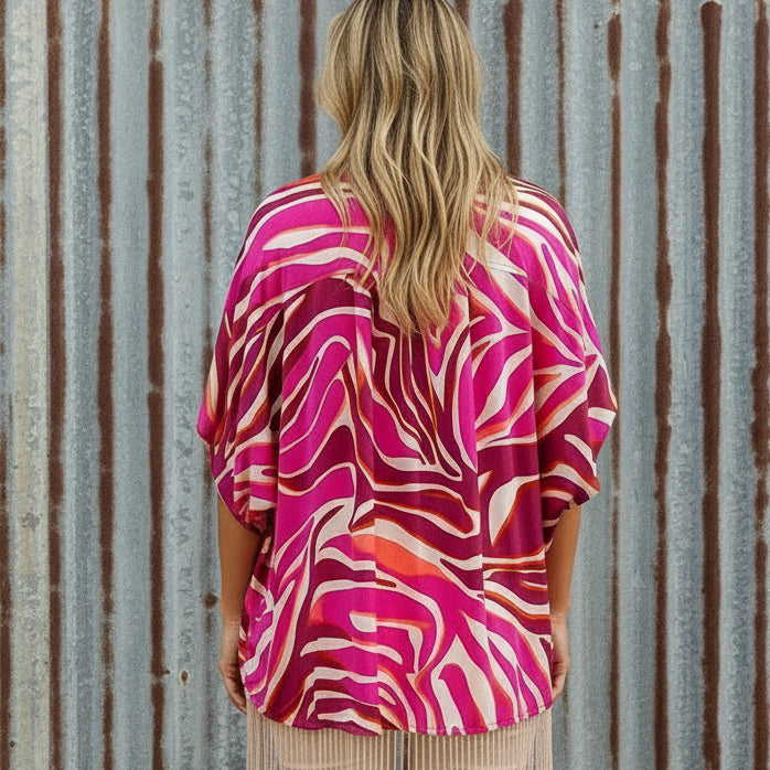 Woman wearing a vibrant pink and orange patterned kimono-style garment in a room setting.